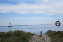 En soppende pige i vandkanten på Ærø med en sejlbåd i baggrunden