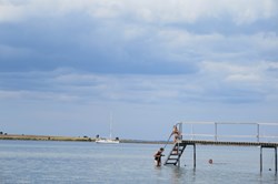 Badende mennesker på Ærø med en sejlbåd i baggrunden