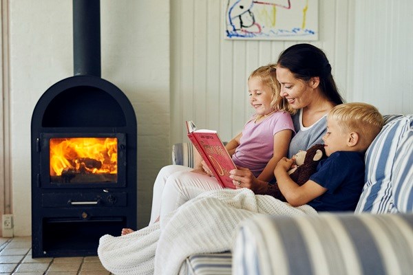 En mor læser højt for sine to børn foran brændeovnen i et hyggeligt sommerhus