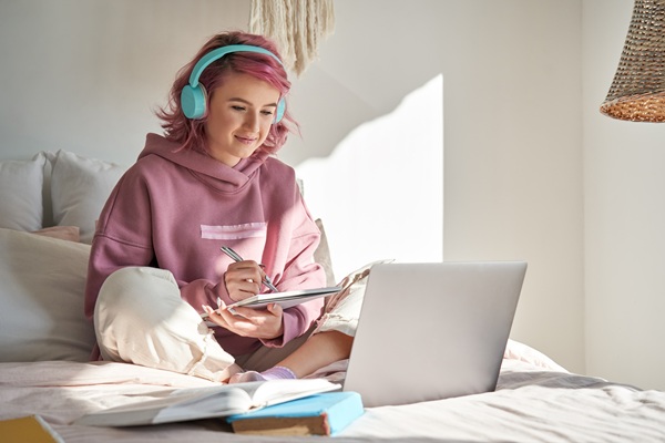 En teenagepige sidder på sengen med høretelefoner og en computer