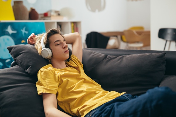 Teenagedreng ligger afslappet på sofaen med høretelefoner og lukkede øjne