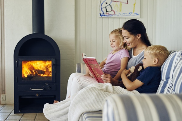 En mor læser højt for sine to børn foran brændeovnen i et hyggeligt sommerhus