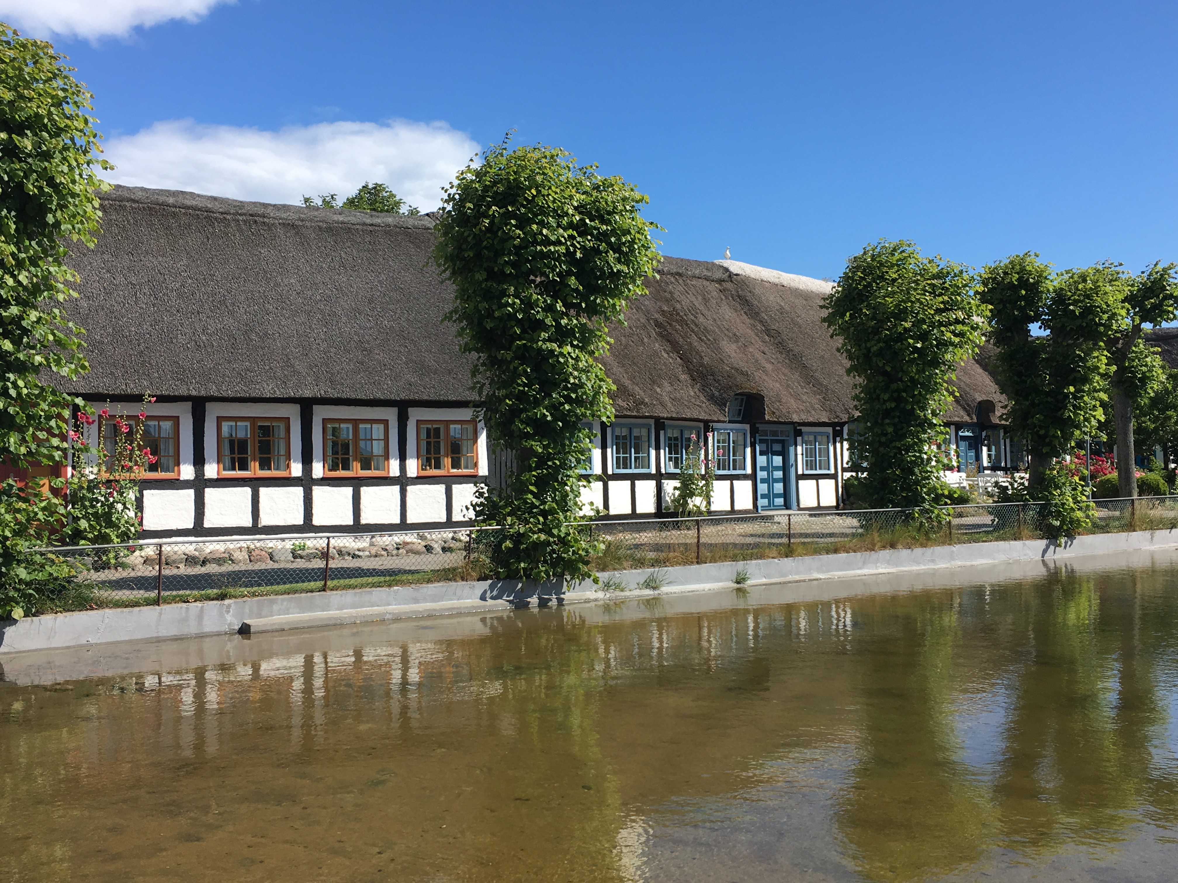 Stråtækt hus i Nordby på Samsø, der spejler sig i søen