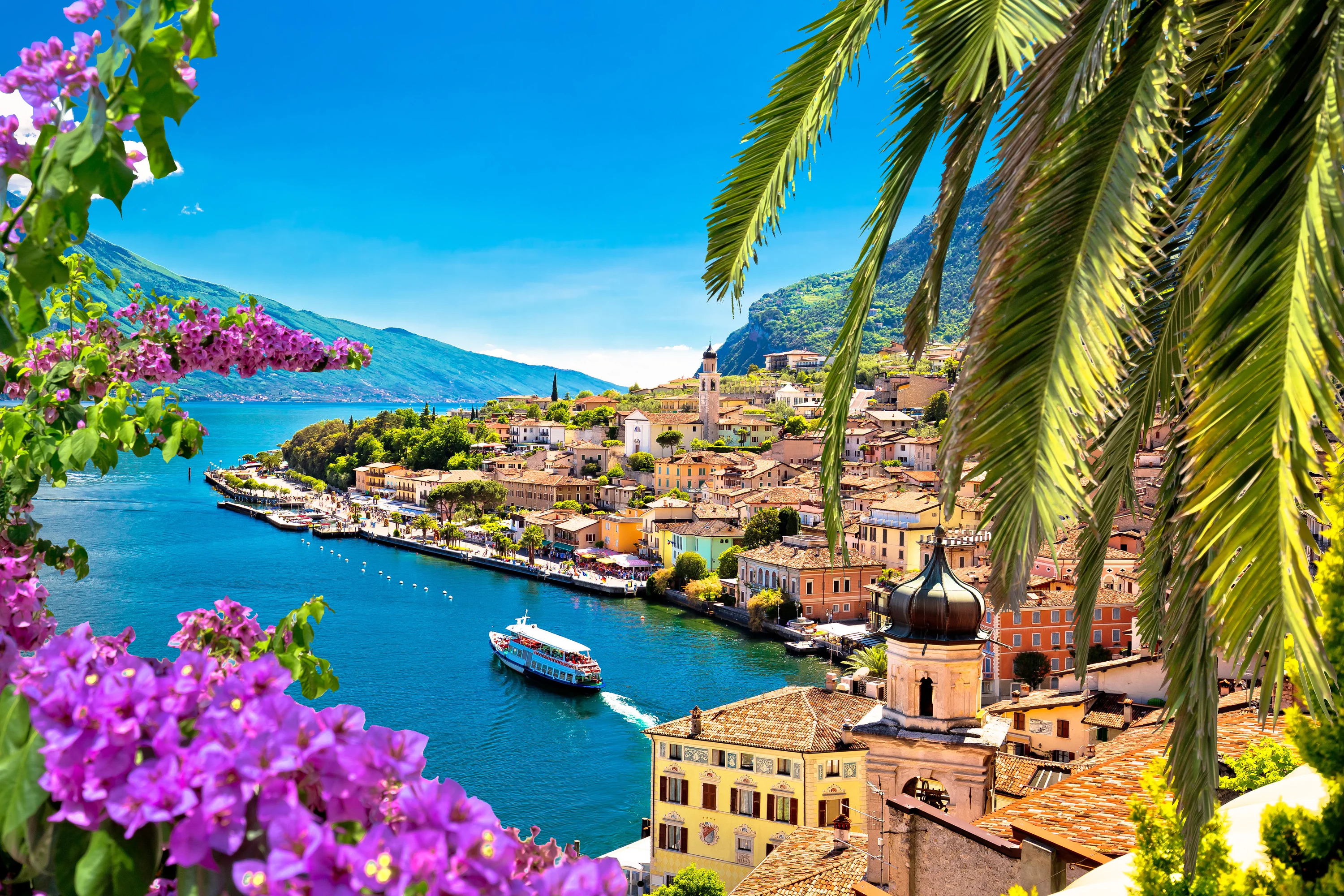 Udsigt over havnefronten i Limone sul Garda gennem blomster og palmetræer i Lombardiet, Italien