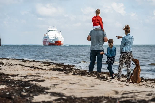 En familie med hund står på stranden og kigger efter FRS Syltfähre